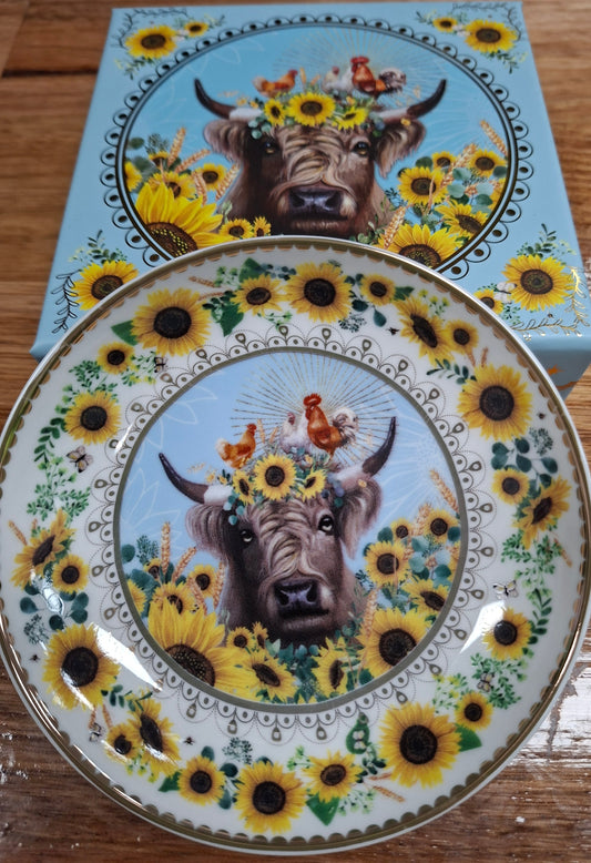 Decorative plate with a cow and sunflower design on a wooden surface