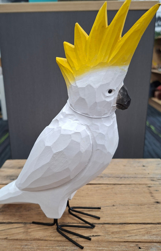 White bird sculpture with yellow crest on a wooden surface