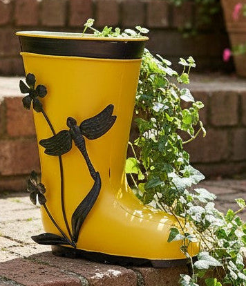 Yellow rain boot with greenery on a stone patio surrounded by potted plants.